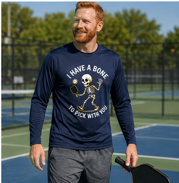 A man on a pickleball court wearing a navy blue long-sleeve graphic shirt with a skeleton and the text 'I HAVE A BONE TO PICK WITH YOU'.