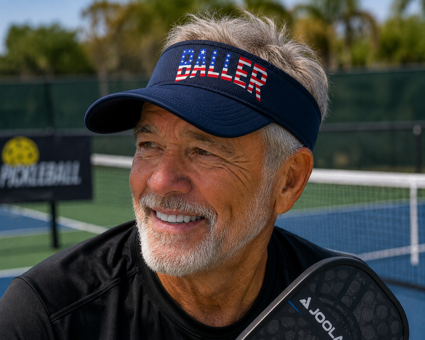"Smiling man wearing a navy BALLER patriotic pickleball visor with American flag lettering on an outdoor pickleball court"