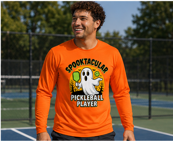 A man wearing a bright orange long-sleeve t-shirt with a 'Spooktacular Pickleball Player' graphic, standing on an outdoor pickleball court.