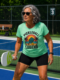 Load image into Gallery viewer, "Model wearing the Tropical Pickleball Legend Palms T-Shirt featuring a retro sunset and palm tree graphic, perfect for pickleball players who love beach vibes"