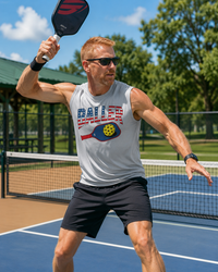 Load image into Gallery viewer, "Man playing pickleball outdoors wearing a sport silver USA Baller patriotic graphic muscle tank, overhead smash on a blue court"