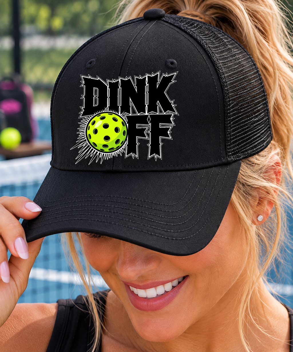 Close-up of a woman wearing a black mesh-back “Dink Off” pickleball micro a hat wnd loop hat with a neon yellow pickleball graphic.