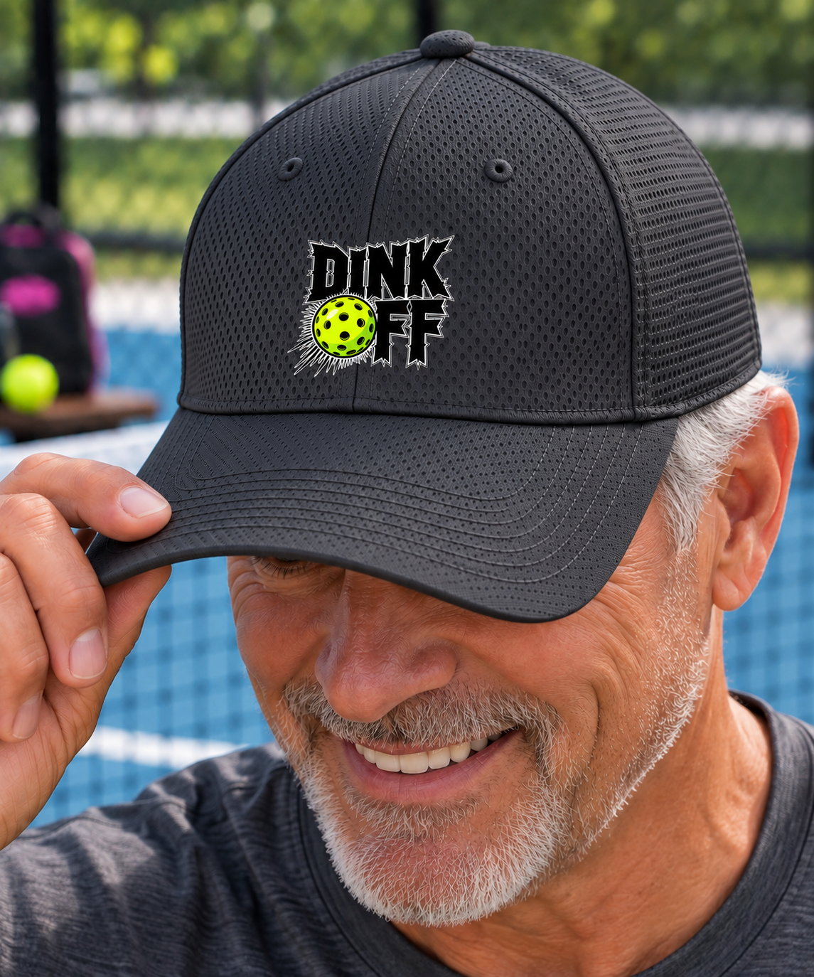 A close-up lifestyle shot of a smiling man wearing a black mesh micro & loop cap with a yellow and black embroidered 'DINK OFF' logo on the front, holding the brim with his hand.