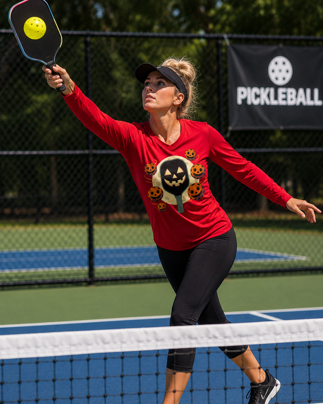 Women's red long sleeve Halloween pickleball shirt worn by woman reaching overhead on outdoor pickleball court, featuring jack-o-lantern paddle and pumpkin pickleball graphic
