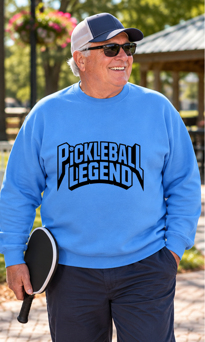 Man wearing a blue sweatshirt with bold black “Pickleball Legend” lettering, sunglasses, and a baseball cap, holding a pickleball paddle outdoors.