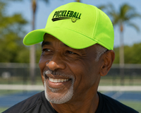 Load image into Gallery viewer, Man wearing a bright green 'Pickleball' streak design on cap with a blurred pickleball court in the background