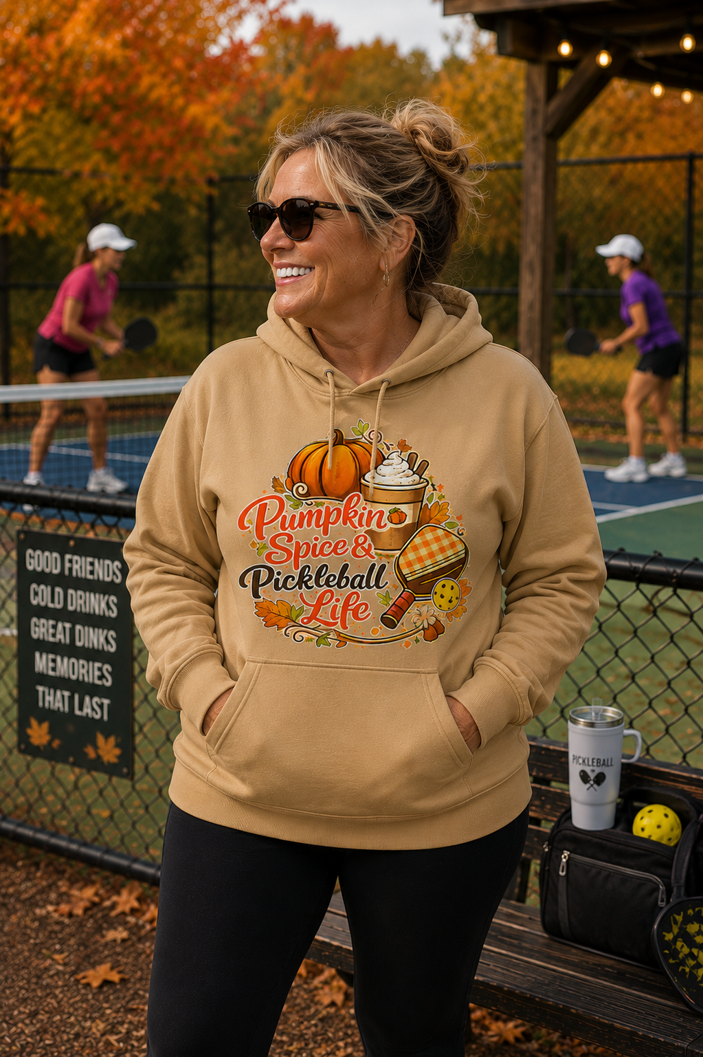 "Woman wearing a tan 'Pumpkin Spice & Pickleball Life' hoodie at an outdoor pickleball court surrounded by fall foliage"