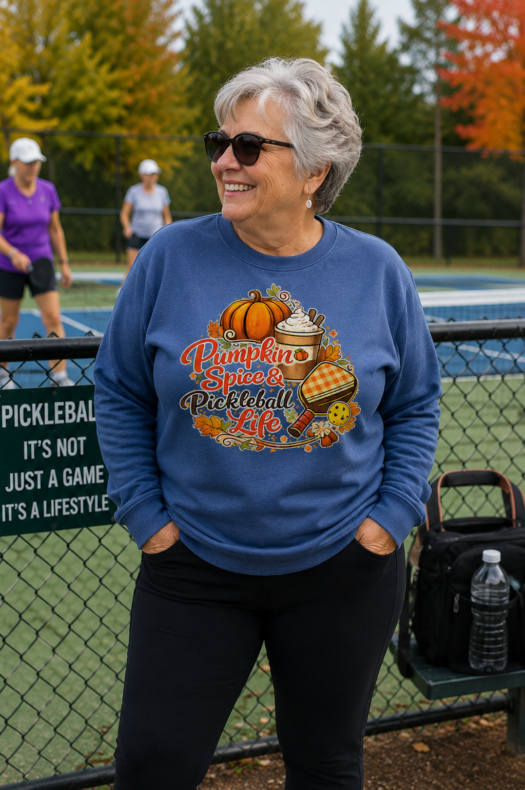 "Woman wearing a blue 'Pumpkin Spice & Pickleball Life' crewneck sweatshirt at an outdoor pickleball court in autumn"