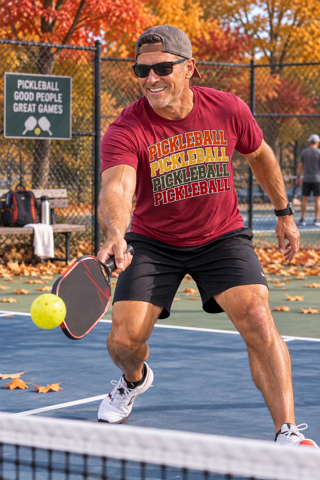 "Man playing pickleball on an outdoor court wearing a antique cherry red Men's Vintage Varsity Stacked Pickleball graphic tee with fall foliage in the background"